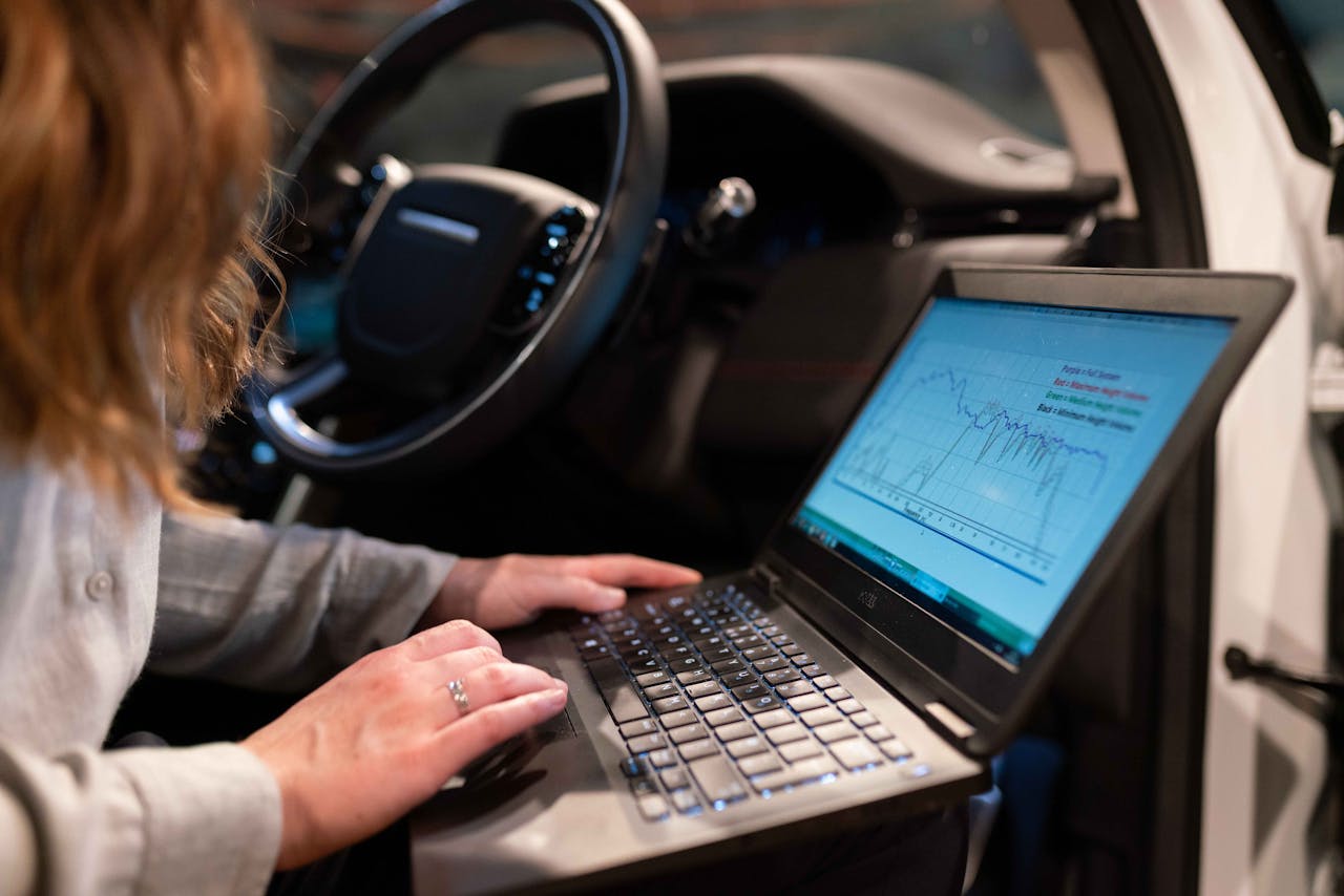 Female engineer using laptop to analyze vehicle data inside a car for testing purposes.